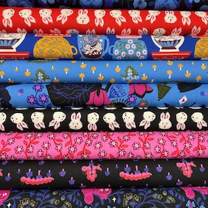 Può includere: Una pila di rotoli di tessuto colorati con vari motivi. I disegni includono conigli, tazze da tè, funghi, fiori e bruchi. I colori includono rosso, blu, nero e rosa. Il tessuto è probabilmente cotone o un materiale simile.