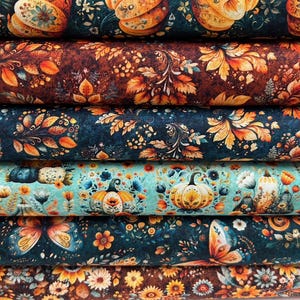 Könnte beinhalten: Ein Stapel Stoffrollen mit herbstlichen Mustern. Die Designs zeigen Kürbisse, Blätter und florale Elemente in Orange-, Braun-, Türkis- und Marineblautönen. Der Stoff scheint weich und strukturiert zu sein.