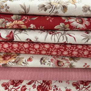May include: A collection of fabric rolls with floral and striped designs. The fabrics showcase diverse patterns, including large flowers, small blossoms, and delicate leaves in red, cream, and beige. The fabrics are neatly stacked, showing a variety of textures.