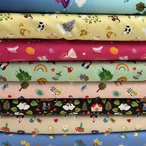 May include: A stack of colorful fabric rolls featuring whimsical patterns. Designs include fairy tale elements like castles, rainbows, pumpkins, and fairies. The fabrics are in various colors, including pink, green, and blue, with a variety of small, repeating illustrations.