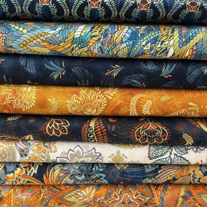 May include: A collection of patterned fabric rolls. The fabrics display detailed designs in shades of blue, orange, yellow, and white. The patterns incorporate floral and paisley elements, offering a visually rich and textured appearance.
