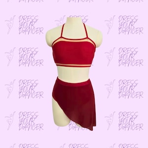 Könnte beinhalten: Ein zweiteiliges Tanzoutfit bestehend aus einem dunkelroten Neckholder-Top mit dünnen Trägern und einem passenden hoch taillierten Rock mit asymmetrischem Saum. Das Set wird auf einer Schaufensterpuppe vor hellviolettem Hintergrund mit Text gezeigt.