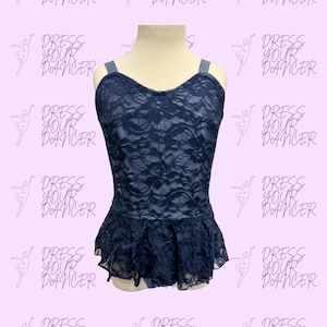 May include: A dark navy blue leotard featuring a floral lace overlay on the bodice and a ruffled peplum skirt at the waist. The garment has wide shoulder straps and a scoop neckline, displayed on a mannequin against a light purple background.