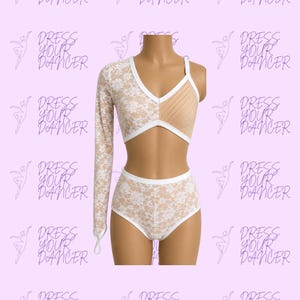 May include: A two-piece dance outfit featuring a white lace long-sleeve crop top with a nude-colored pleated panel on one side and a matching white lace high-waisted bottom. The top has a white trim and a single long sleeve with a finger loop.