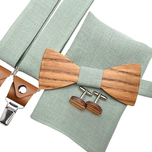Puede incluir: Un conjunto de pañuelo de bolsillo, pajarita y tirantes de lino verde claro, con una pajarita de madera y gemelos a juego. La pajarita y los gemelos son de madera con un patrón de vetas natural.