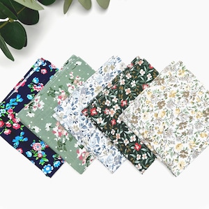 Könnte beinhalten: Eine Sammlung gefalteter Taschentücher mit floralen Mustern. Die Taschentücher weisen verschiedene Farben auf, darunter Marineblau, Grün, Weiß und Dunkelgrün, mit floralen Designs in Rosa-, Blau- und Gelbtönen. Die Taschentücher sind fächerförmig angeordnet.