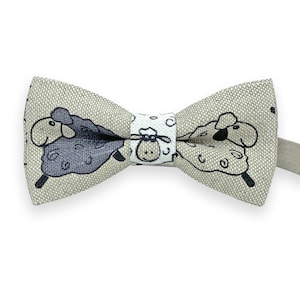 Può includere: Un papillon beige con un motivo di pecore bianche e nere. Il papillon ha una pecora bianca e nera da un lato e una pecora bianca dall'altro.