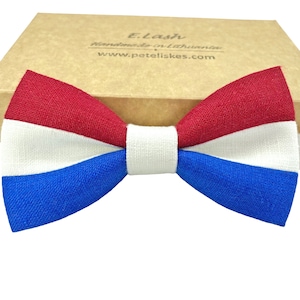 May include: A red, white and blue bow tie made of fabric. The bow tie is in the shape of the Dutch flag.