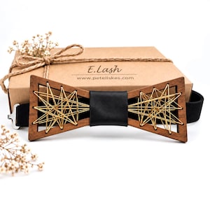 Può includere: Un papillon in legno con cornice marrone scuro, motivi geometrici a stella realizzati con filo dorato su entrambi i lati e un inserto centrale in pelle nera. Il papillon è fissato a un cinturino elastico nero davanti a una scatola regalo.
