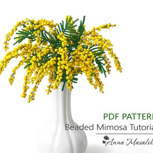 Può includere: Un modello PDF per un tutorial di bouquet di fiori di mimosa perlati. L'immagine mostra un vaso bianco con un bouquet di fiori di mimosa gialli con foglie verdi.