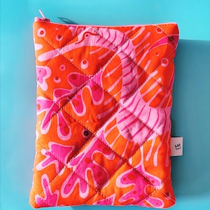 May include: Quilted orange and pink patterned pouch with a zipper closure. The pouch features a repeating abstract design in shades of orange and pink. A small white tag with a crown logo is attached to the side. The background is a solid turquoise color.