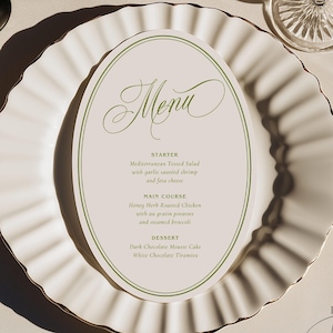 May include: An oval menu card with green text and border, featuring the word Menu in script, placed on a white scalloped dinner plate. The menu lists starter, main course, and dessert options. A fork and knife are positioned on the sides.