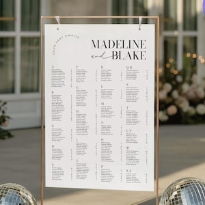 May include: A wedding seating chart with the names "Madeline and Blake" printed on a white card. The card is suspended within a copper-colored metal frame. Silver disco balls are arranged at the base of the frame.