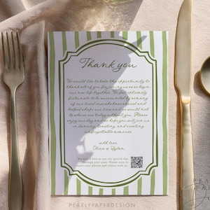 May include: A wedding thank you card with a green and white striped border and elegant script. The card is placed on a beige tablecloth next to gold cutlery and a vase of flowers. The card reads "Thank you".