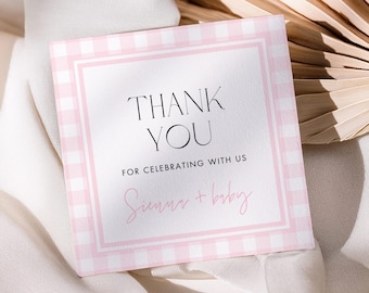 Peut inclure: Une carte de remerciement carrée avec un motif vichy rose et blanc. Le texte "THANK YOU" et "FOR CELEBRATING WITH US" est présent. Les noms "Sumus + baby" sont écrits en cursive. La carte est posée sur un tissu blanc et une feuille de palmier séchée.