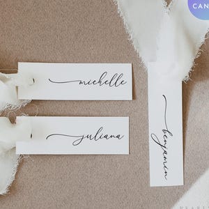 May include: White rectangular place cards with names Michelle, Juliana, and Benjamin in elegant black script. The cards are tied with white ribbons, set against a neutral background. The words "Edit with Canva" are in a circle.