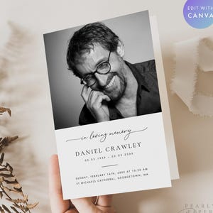 May include: A black and white memorial card held in a hand. The card features a photograph of a smiling man wearing glasses. Text on the card reads "in loving memory" and the name "DANIEL CRAWLEY" with dates and a location.
