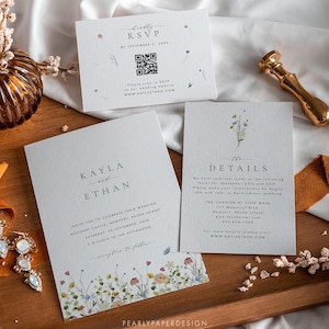 May include: Wedding invitation suite featuring floral accents and elegant typography. Includes an invitation, RSVP card with a QR code, and details card. The suite is displayed on a wooden tray with a gold wax seal and decorative elements.