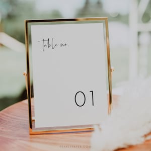 以下が含まれることがあります： 「Table no.」というテキストと黒い数字「01」が書かれた、金色のフレームのテーブル番号札です。