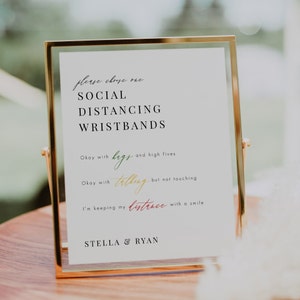 May include: A gold-framed sign with the text "Please choose one: Social Distancing Wristbands."  The sign lists three options: "Okay with hugs and high fives", "Okay with talking but not touching", and "I'm keeping my distance with a smile." The sign is signed "Stella & Ryan".