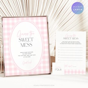 May include: A framed sign with a pink and white gingham pattern, featuring the text "Guess the Sweet Mess." Accompanied by a game card and small cards. The sign invites guests to identify the candy bar.