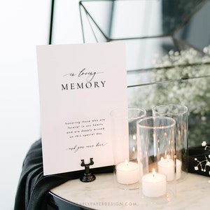 May include: A white sign with black text that reads "in loving memory" and "honoring those who are forever in our hearts and are deeply missed on this special day. wish you were here." The sign is sitting on a black table with a black cloth and four glass candle holders with white candles.