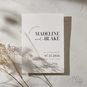 May include: A minimalist save the date card with a white background and black text. The text reads "Save Our Date" in a circle, followed by "Madeline and Blake" in a bold font. The date "07.25.2026" is printed below, along with the location "Newport, Rhode Island". The text "formal invitation to follow" is written in cursive at the bottom.