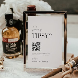 May include: A white sign with black text and a QR code that reads "Feeling Tipsy? Leave a tip for your bartender, scan the code or leave cash. With love, Ashley & Jerome."