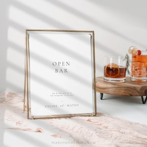 Op de afbeelding: Een gouden lijst met de tekst "OPEN BAR" en de boodschap "the drinks are on us, the hangover is on you!"  Het bord bevat ook de namen "CELINE & MATEO".