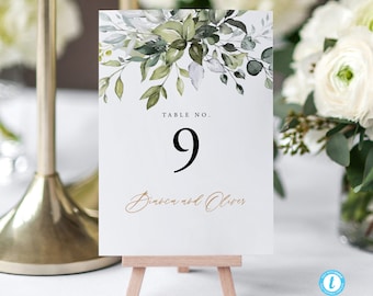 Op de afbeelding: Witte kaart met een aquarelontwerp van groene bladeren en een gouden inscriptie met de tekst "Tafel Nr. 9 Bianca en Oliver".