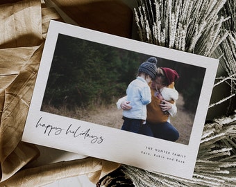 May include: A Christmas card with a photo of a family of three in a wooded area. The card reads "happy holidays" and "The Hunter Family, Sara, Rubin and Rose".