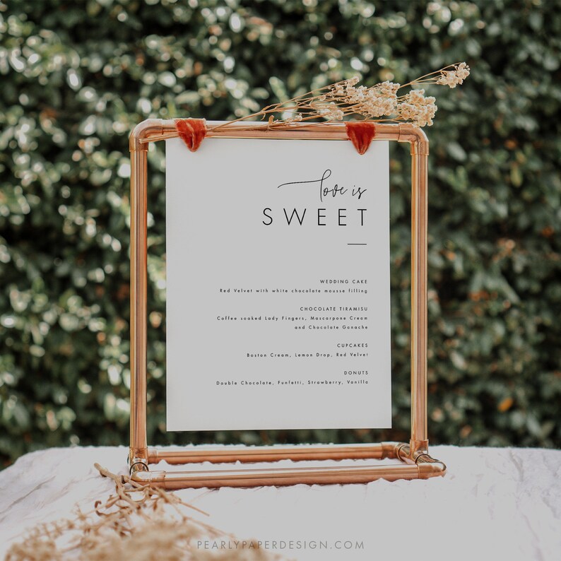Puede incluir: Un cartel blanco con el texto "Love is Sweet" en un soporte de tuber&iacute;a de cobre. El cartel enumera pastel de bodas, tiramis&uacute; de chocolate, cupcakes y donas.