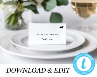 Könnte beinhalten: Weiße Tischkarte mit schwarzem Text, der "VICTORIA ADAMS Tisch eins" lautet, und einer kleinen schwarzen Silhouette einer Kuh in der oberen rechten Ecke.