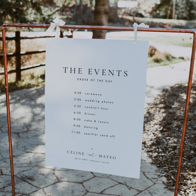 Puede incluir: Un cartel blanco con texto negro que enumera el orden de los eventos de una boda. El cartel est&aacute; colgado de un marco de tuber&iacute;a de cobre. El texto dice: "THE EVENTS ORDER OF THE DAY 4:00 ceremony 5:00 wedding photos 5:30 cocktail hour 6:30 dinner 8:00 cake & toasts 9:00 dancing 11:00 sparkler send off CELINE & MATEO 08.21.2021 Balcoart Castle"
