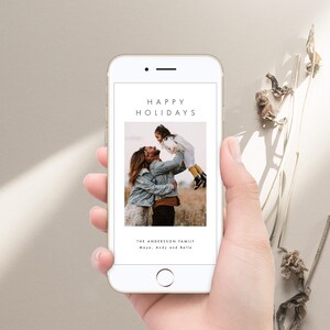 May include: A smartphone displaying a digital holiday card with a photo of a family of three. The text on the card reads "Happy Holidays" and "The Andersson Family Maya, Andy and Belle".