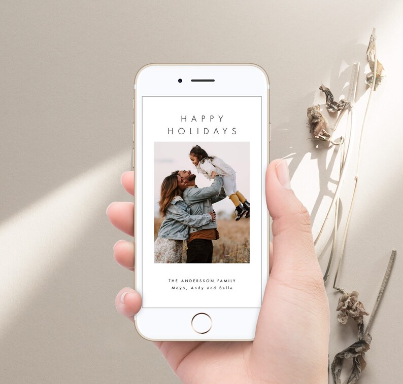May include: A smartphone displaying a digital holiday card with a photo of a family of three. The text on the card reads "Happy Holidays" and "The Andersson Family Maya, Andy and Belle".