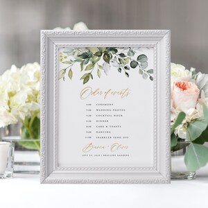 May include: A white framed sign with a watercolor illustration of green leaves and the text "Order of Events" in gold script. The sign lists the wedding day schedule with times and events, including ceremony, wedding photos, cocktail hour, dinner, cake and toasts, dancing, and sparkler send off. The names "Diarca Oliver" and the date "July 25, 2020" are also included in gold script. The sign is perfect for a wedding reception.