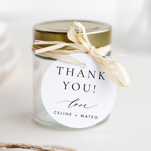 May include: White round thank you tag with the text "Thank You! Love Celine + Mateo" tied to a clear glass jar with a gold lid and a beige ribbon.