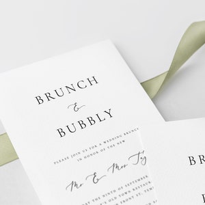 May include: A white wedding invitation with black text that reads "BRUNCH & BUBBLY" and "PLEASE JOIN US FOR A WEDDING BRUNCH IN HONOR OF THE NEW Mr & Mrs Ty". The invitation also includes the date "DAY THE NINTH OF SEPTEMBER" and the location "Y'S OLD TOWN RESTAURANT, FRONT ST, TEMI".