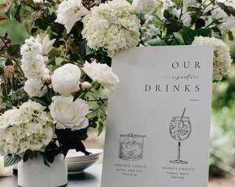 Könnte beinhalten: Ein weißes Schild mit dem Text "OUR signature DRINKS" und Cocktail-Illustrationen. Das Schild enthält den Text "GROOM'S CHOICE" und "BRIDE'S CHOICE" mit Zutaten. Weiße Blumen und Grünzeug sind im Hintergrund arrangiert.