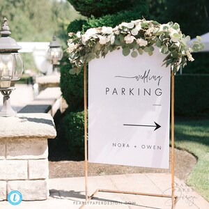 May include: White wedding parking sign with black text and arrow. The sign reads "wedding parking" with a line underneath and an arrow pointing to the right. Below the arrow, it reads "Nora + Owen".
