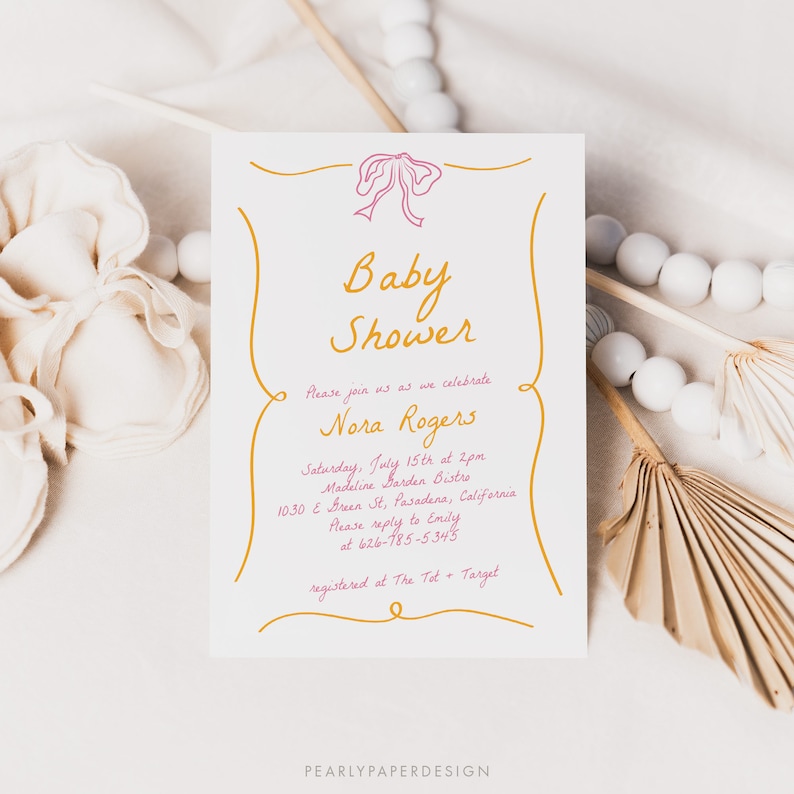May include: A white baby shower invitation with gold and pink lettering. The invitation reads "Baby Shower" and includes the name "Nora Rogers". The invitation details the date, time, location, and RSVP information. The invitation also includes the text "registered at The Tot + Target".