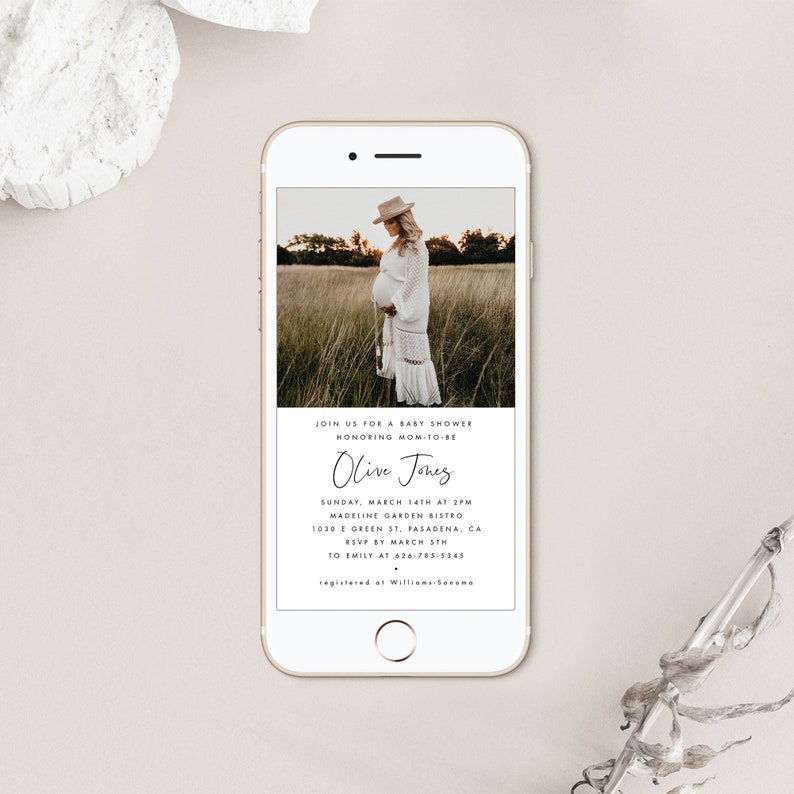 May include: A white and gold phone screen displaying a baby shower invitation for Olive Jones. The invitation includes the date, time, location, and RSVP information. A photo of a pregnant woman in a white dress is in the background.