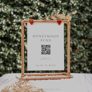 May include: A white sign with the text "Honeymoon Fund" and a black QR code. The sign is displayed on a copper pipe stand with a red velvet ribbon. The text "Thank you for celebrating with us" and "Celine & Mateo" is also on the sign.