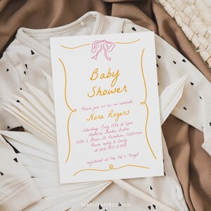May include: A baby shower invitation with a pink bow and gold lettering. The invitation reads "Baby Shower" and "Please join us as we celebrate Nora Rogers". The event is scheduled for Saturday, July 15th at 2pm at Madeline Barden Bistro in Pasadena, California. The invitation also includes a phone number and registry information.