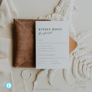 May include: A white RSVP card with black text that reads "Kindly Reply by [date]" with a section for name, RSVP options, and dietary requirements. The card is on a brown textured surface with a white wax seal.