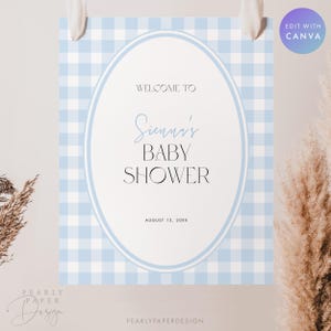 May include: A baby shower sign with a light blue gingham pattern background. The sign has an oval frame with the words "Welcome to Sienna's Baby Shower" and the date "August 15, 20XX". The sign is hanging from white ribbons.