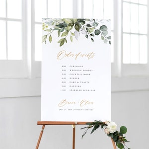 May include: A white wedding sign with gold lettering and green foliage. The sign lists the order of events for a wedding, including the ceremony, wedding photos, cocktail hour, dinner, cake and toasts, dancing, and sparkler send off. The sign also includes the couple's names, Bianca and Oliver, and the date and location of the wedding.