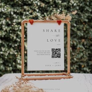 Könnte beinhalten: Ein weißes Schild mit einem Kupferrahmen, auf dem der Text "SHARE the LOVE" und ein QR-Code zu sehen sind. Das Schild enthält auch den Text "PLEASE SCAN THIS QR CODE TO UPLOAD AND SHARE YOUR PHOTOS WITH US" und die Namen "ISSA + JAKE".