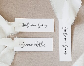 May include: Three white rectangular place cards with black calligraphy. The top card reads "Julianna Jones", the middle card reads "Simone Wallis", and the bottom card reads "Julianna Jones".